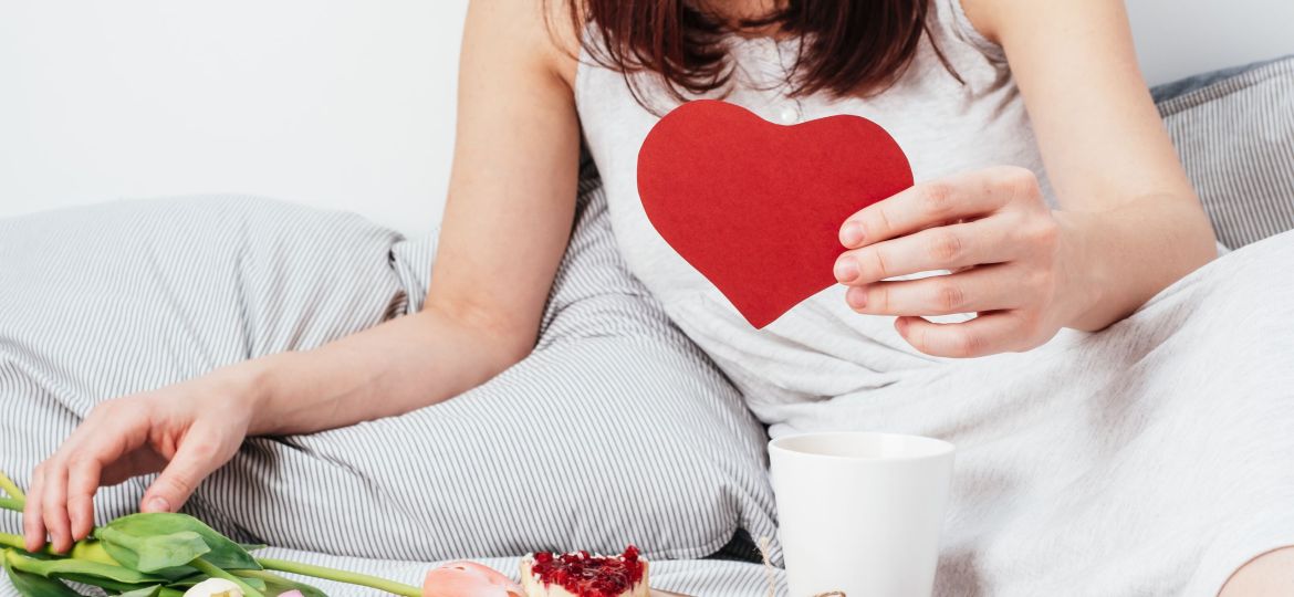 The girl is holding a red heart. Congratulations on Valentine's Day on February 14. Breakfast in bed and a gift.
